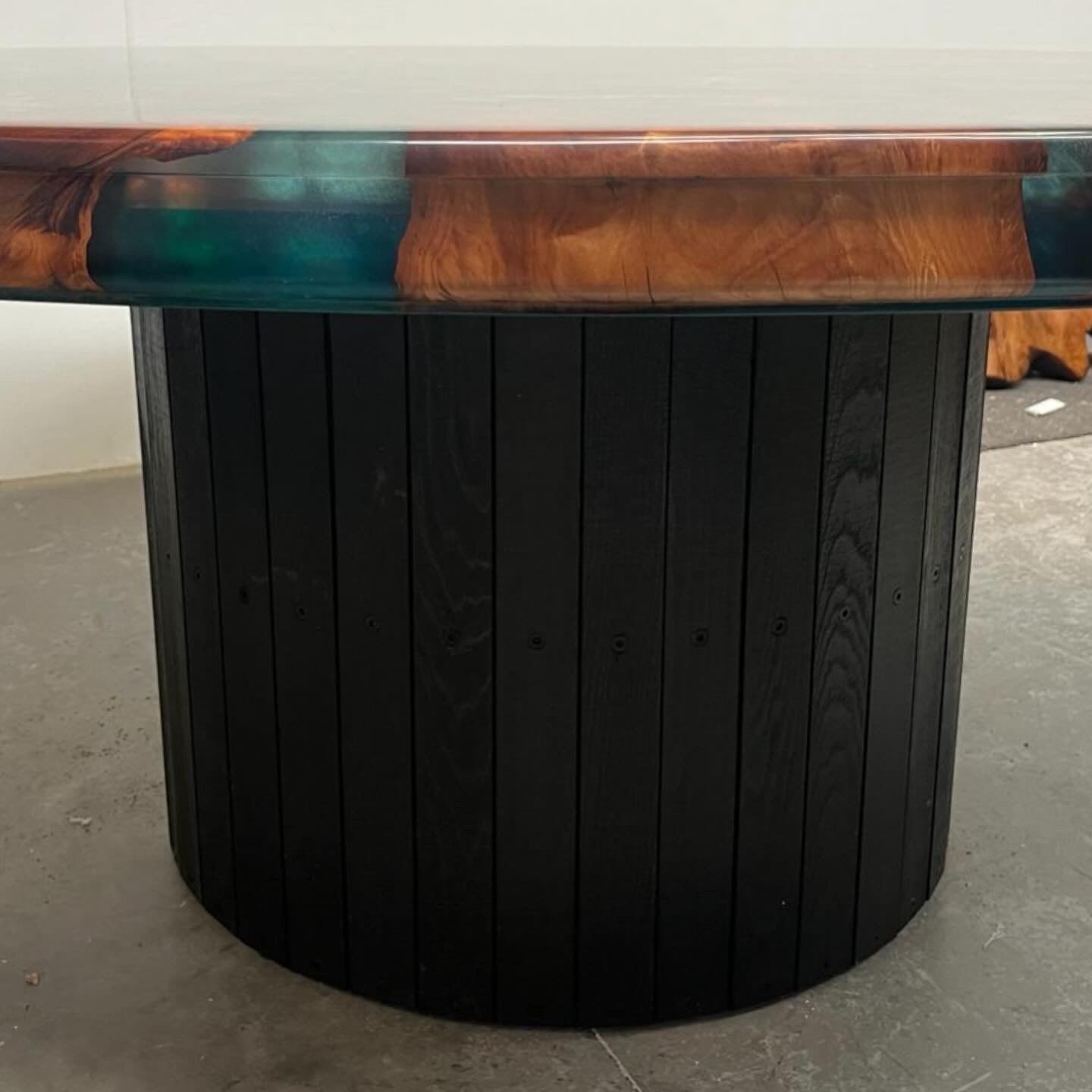 Edge of a round swamp kauri table with green metallic resin on a black pedestal base
